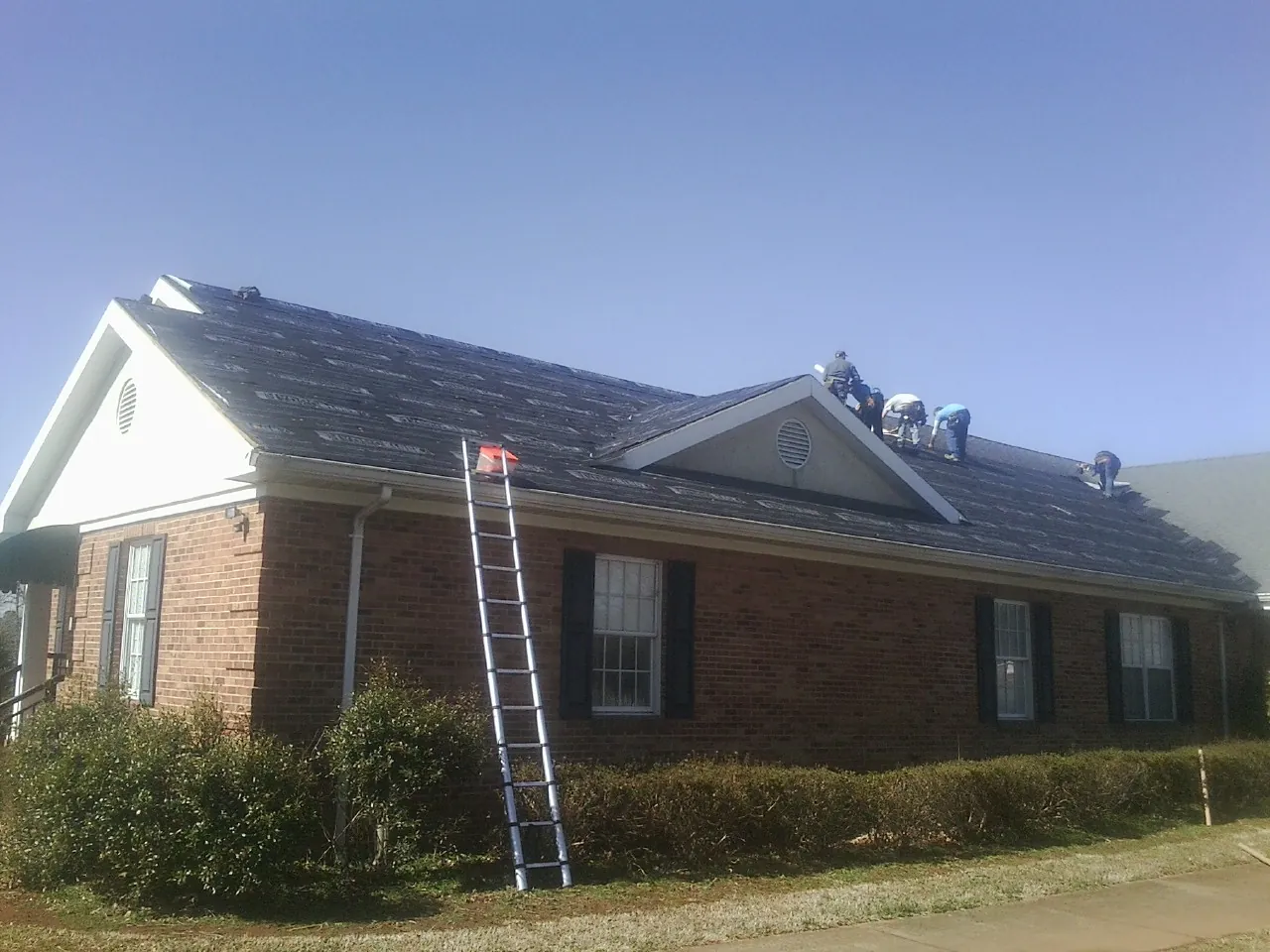 Crew tearing shingles off a brick ranch roof with a ladder set — Emergency Roof Repair work by our crew in Due West