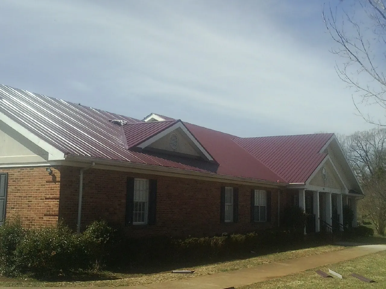 Red metal roof with gabled entries on a long brick building, from a Hail Damage Roof Repair job in Due West