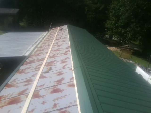 Old rusted panels beside newly installed green metal roofing — Wind Damage Roof Repair by Roofing Brothers in Due West