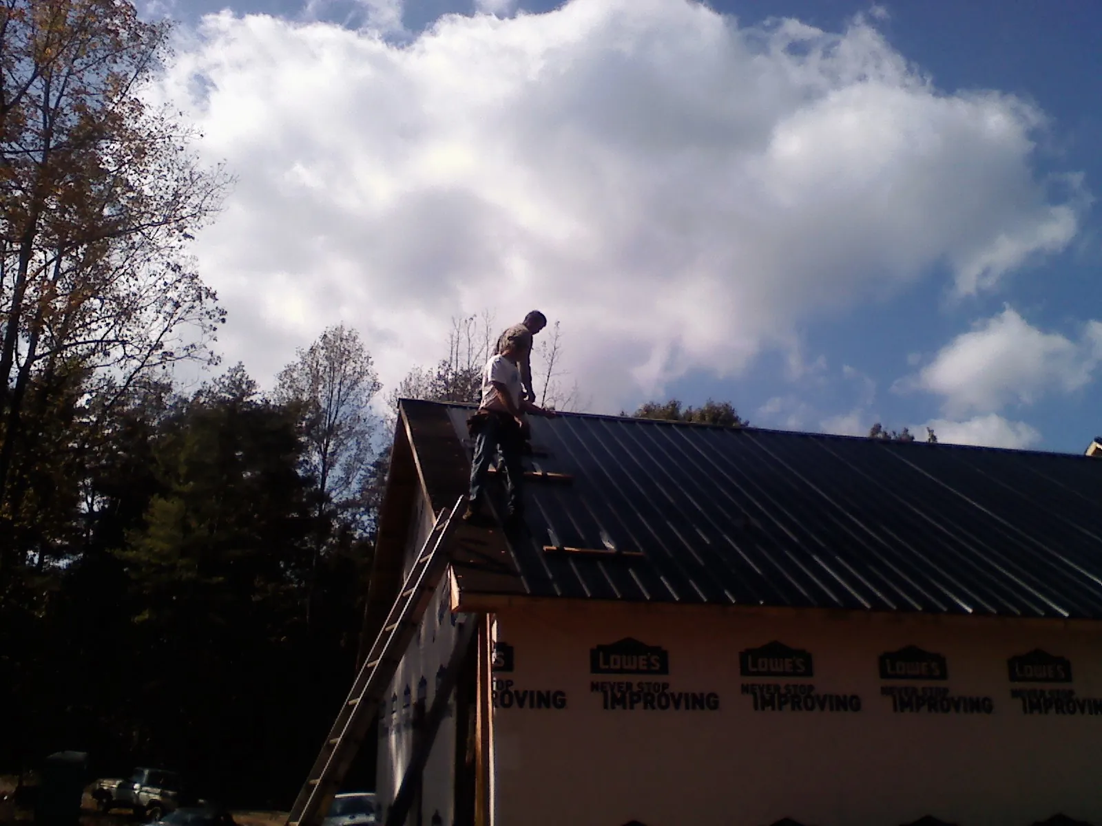 Roofer fastening dark metal panels high against a cloudy sky, from a Roof Inspection job in Due West