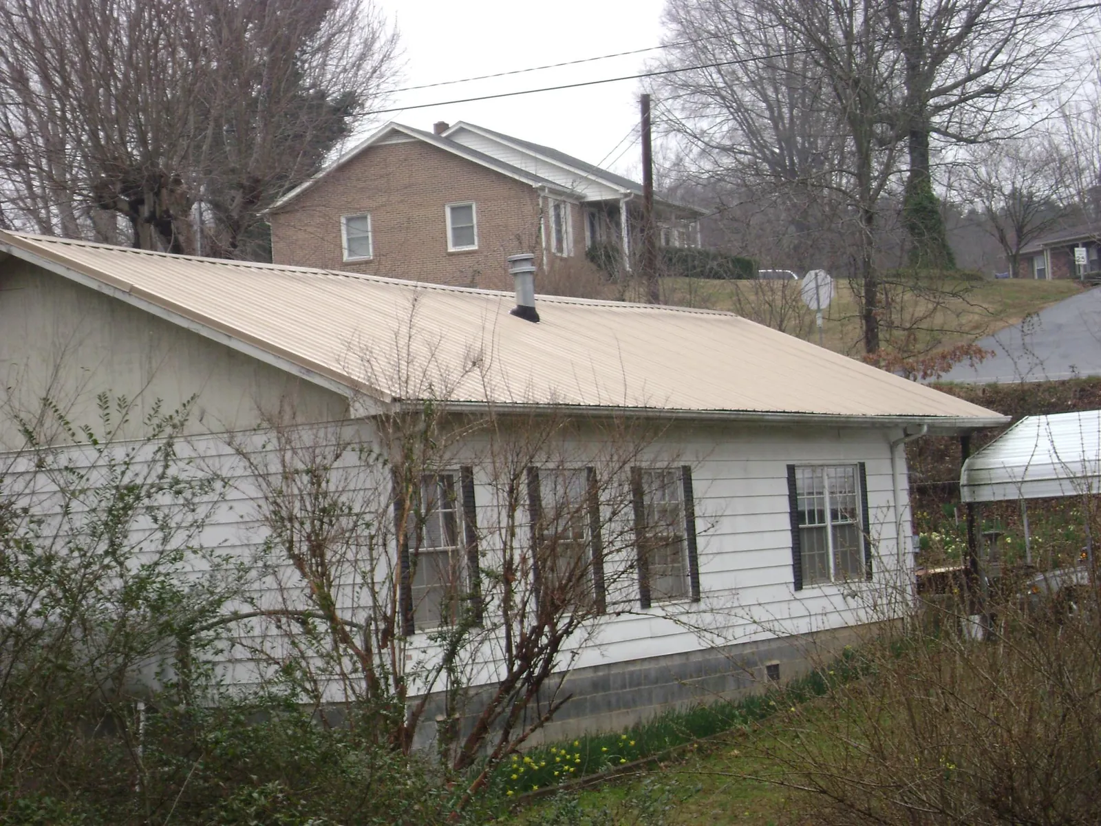 Tan metal roof on a white sided house set into a hillside — Commercial Roofing by Roofing Brothers in Due West